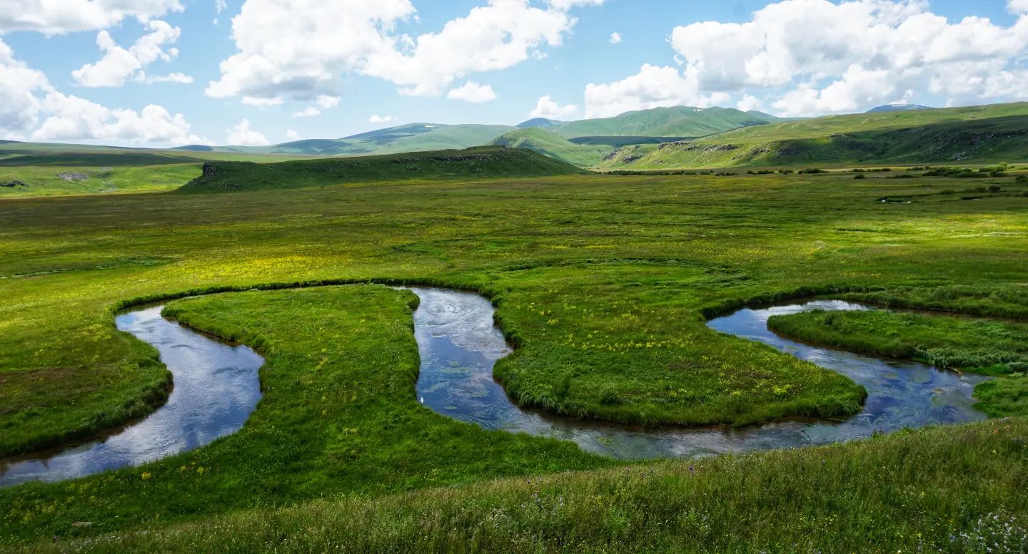 A photo of a river meandering through the grassy landscape of the Gegham Mountains.