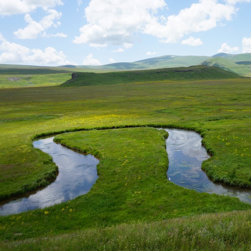 A photo of a river meandering through the grassy landscape of the Gegham Mountains.