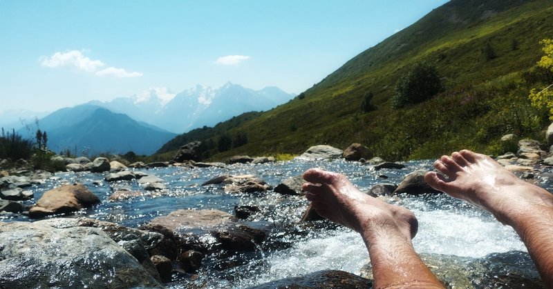Una fotografía tomada en un arroyo cerca del nivel del agua, mirando los pies del excursionista con montañas al fondo.