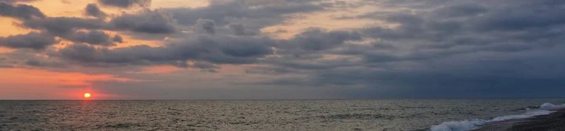 A short, wide photograph of the sun setting into the Black Sea viewed from the beach at Anaklia, the northern end of the Transcaucasian Trail.